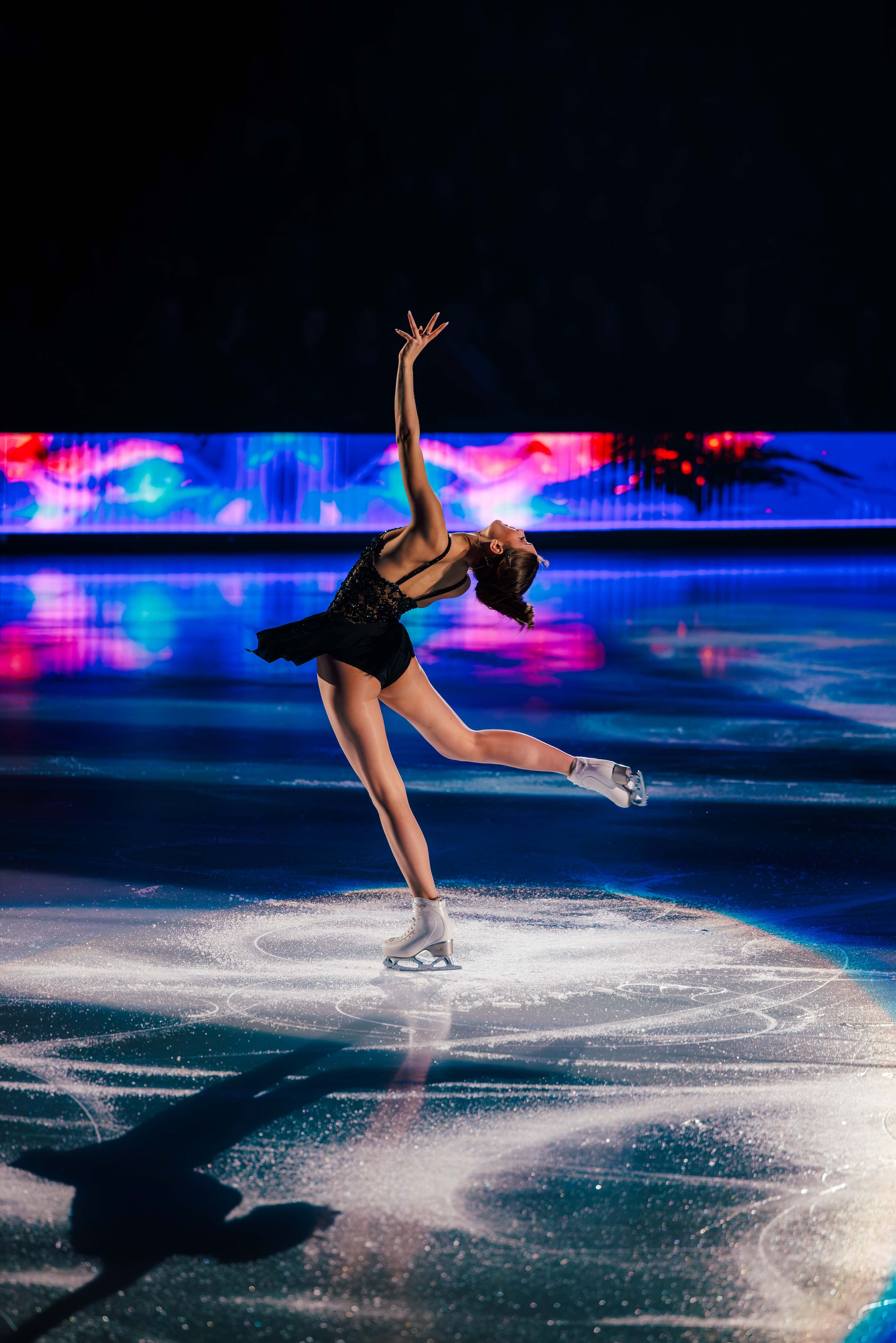 Eine Eiskunstläuferin in schwarzem Kleid gleitet in perfekter Pose über das Eis.
