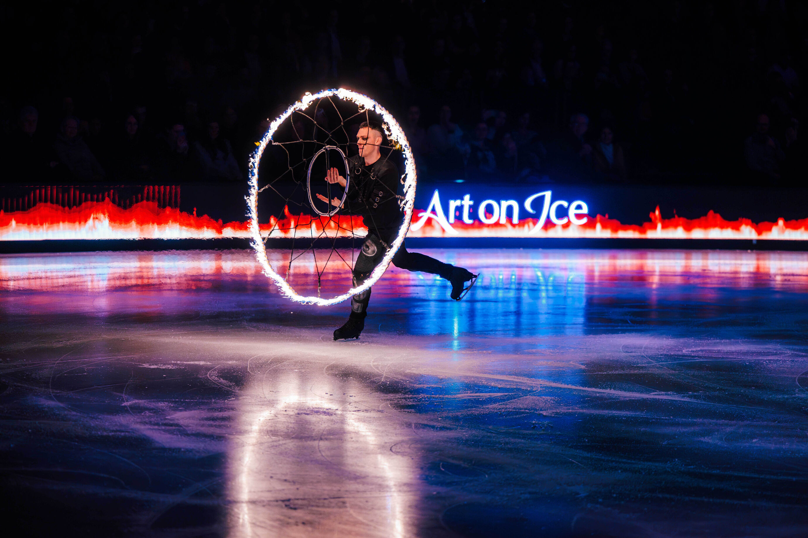 Ein Artist rollt mit brennendem Reifen über das Eis.