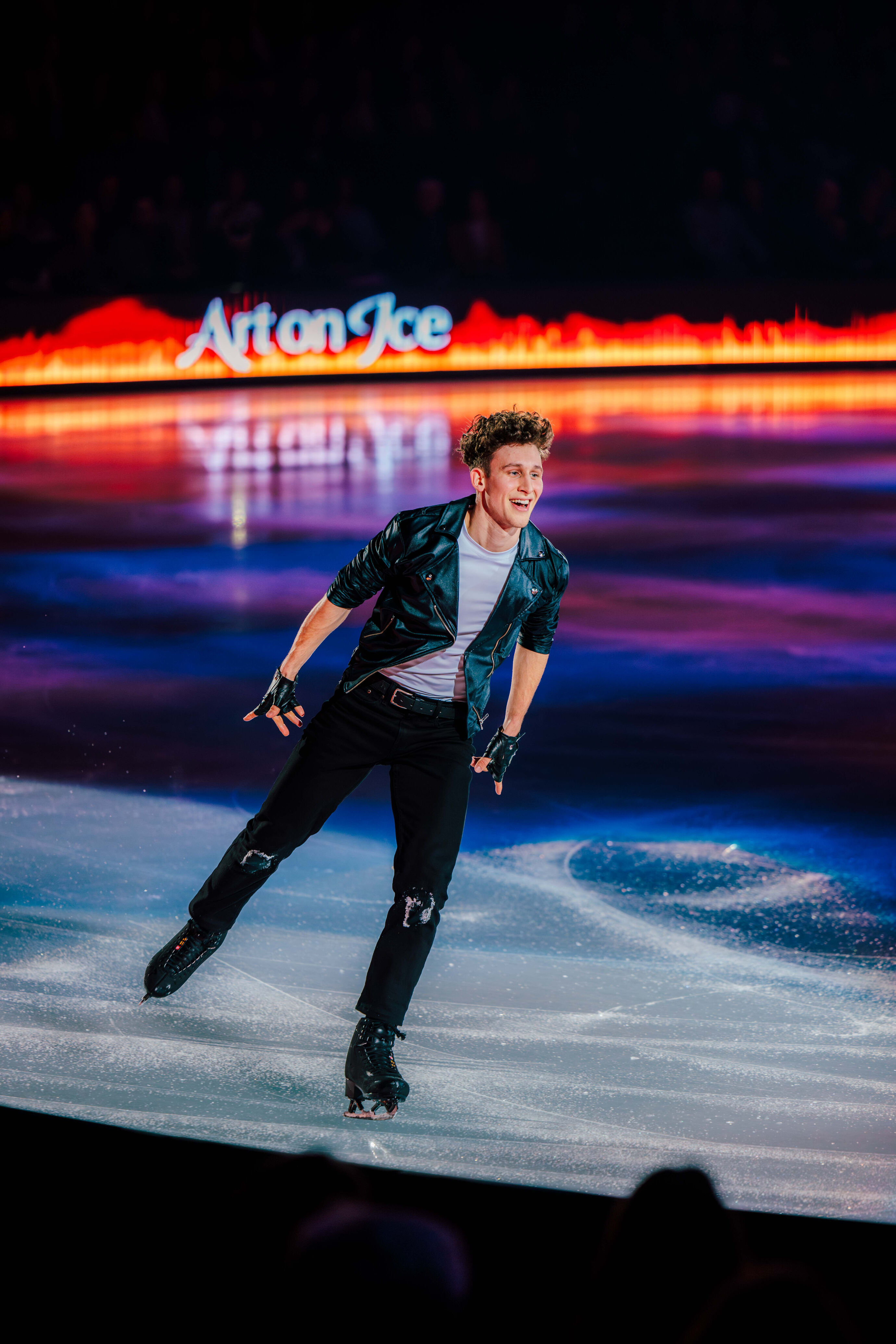 Ein Eiskunstläufer in schwarzer Lederjacke fährt schwungvoll übers Eis.