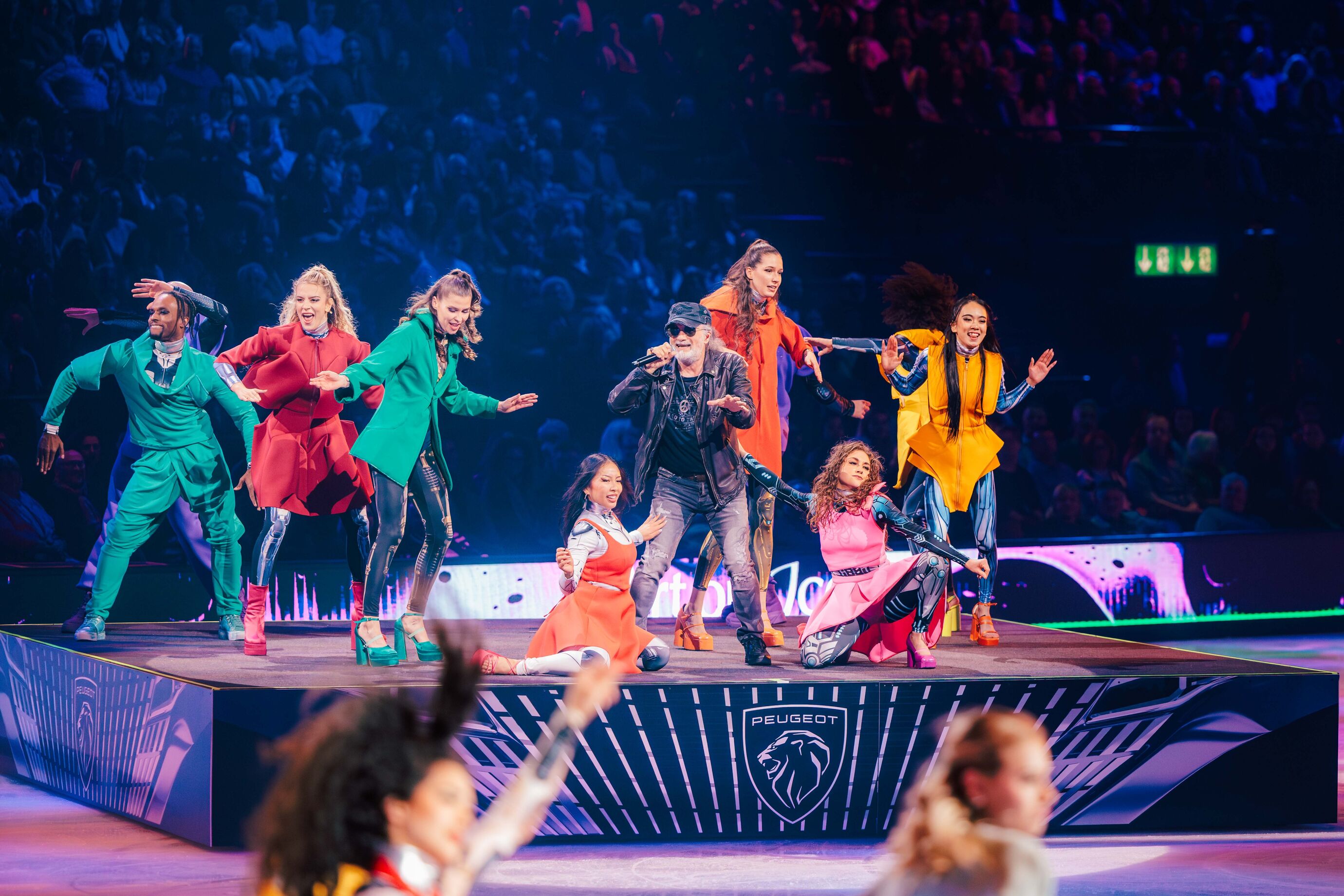 Tänzer in farbenfrohen Kostümen performen gemeinsam auf der Eisfläche.