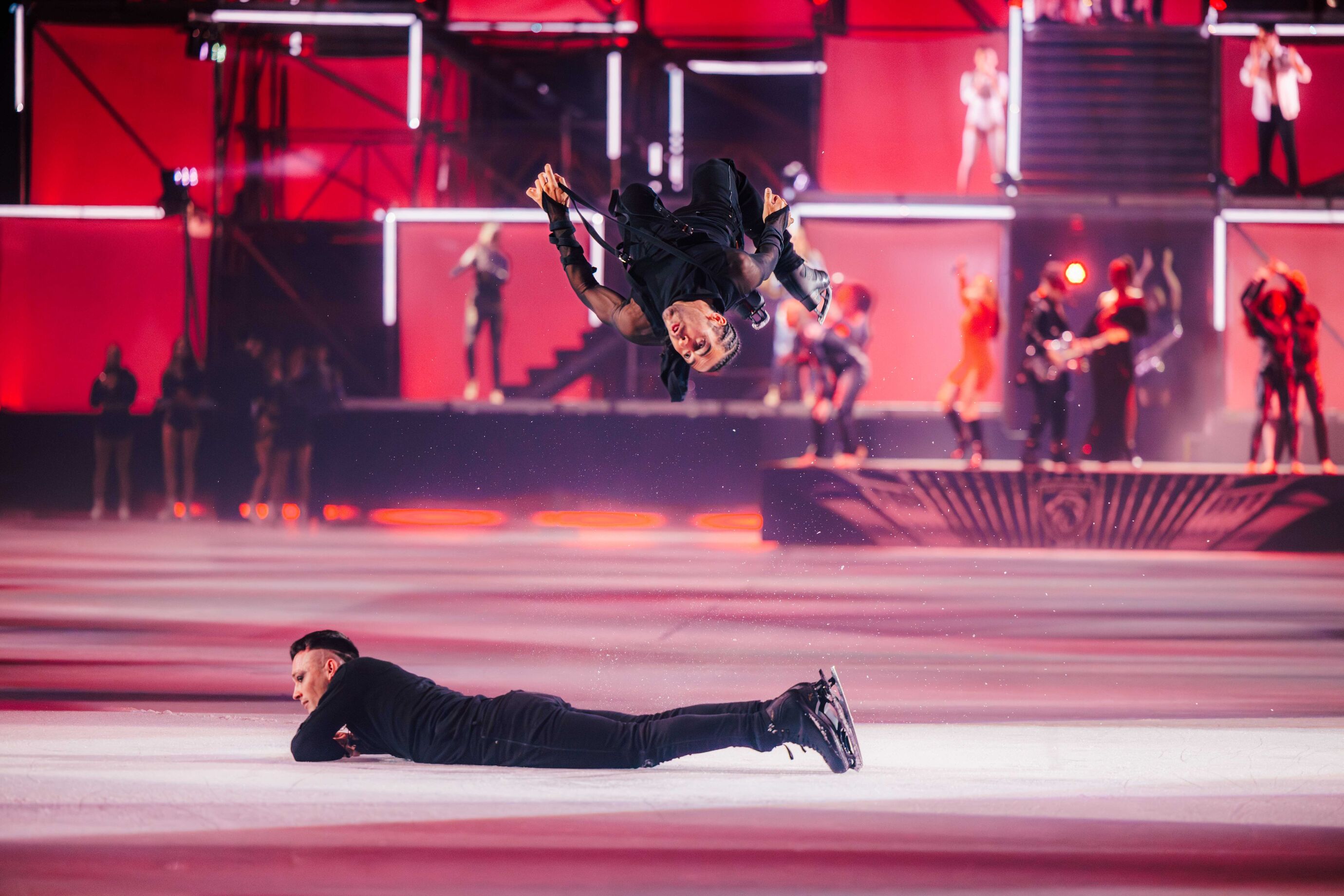 Ein Eiskunstläufer überschlägt sich artistisch über dem Eis, begleitet von einer Showeinlage.