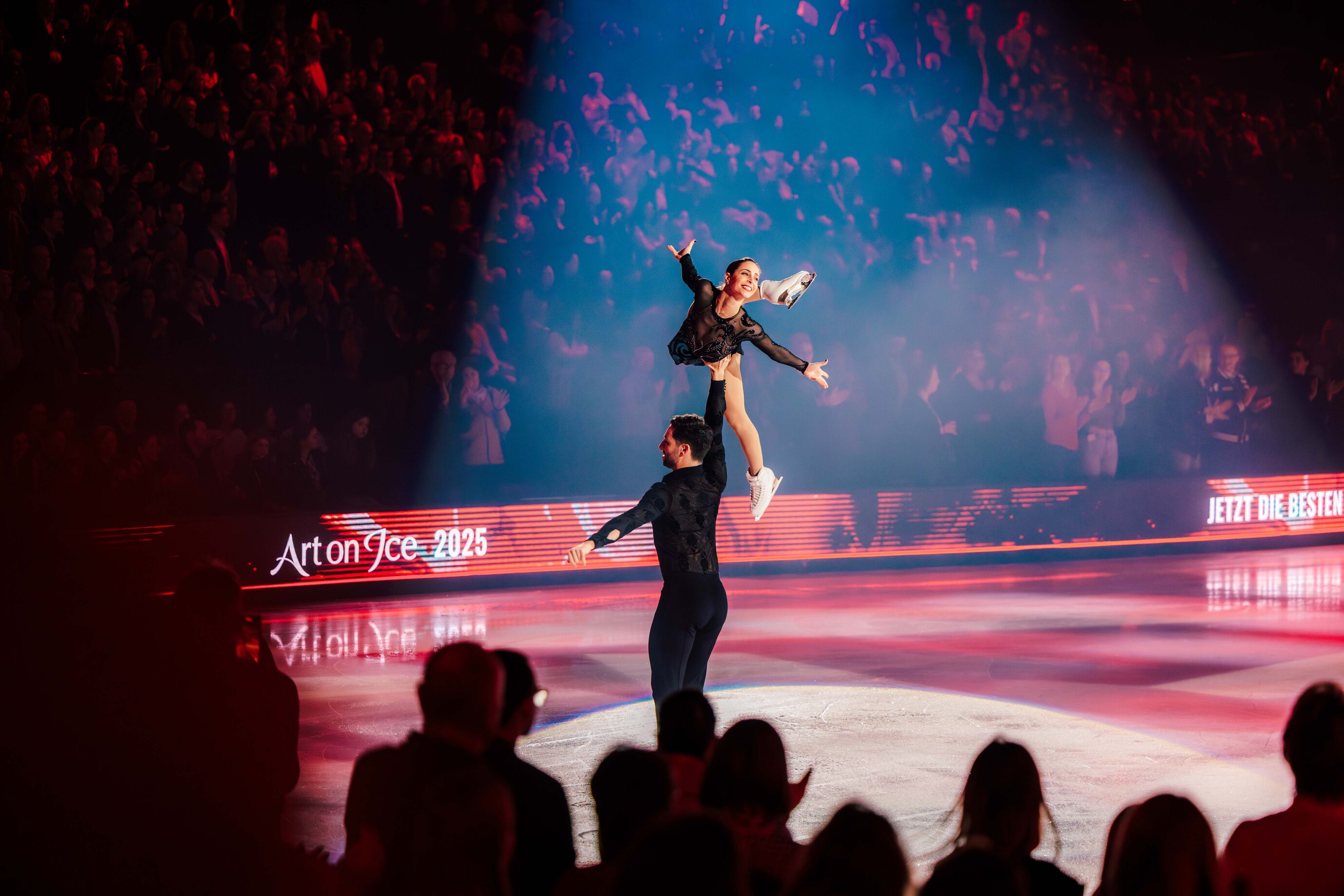 Ein Eiskunstläufer hebt seine Partnerin hoch über den Kopf.
