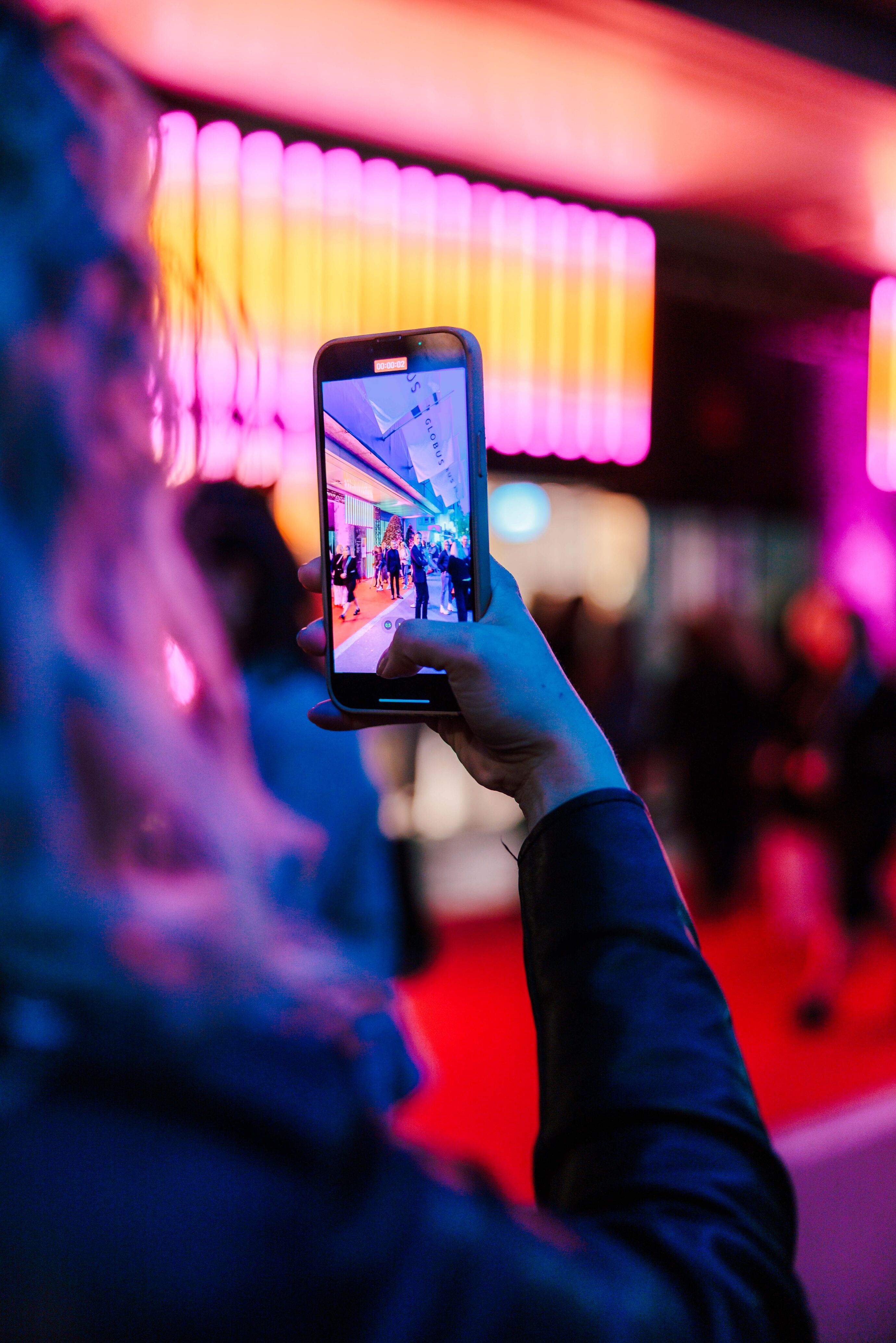 Eventfotograf Zürich – Gast fotografiert Event mit Smartphone im Neonlicht