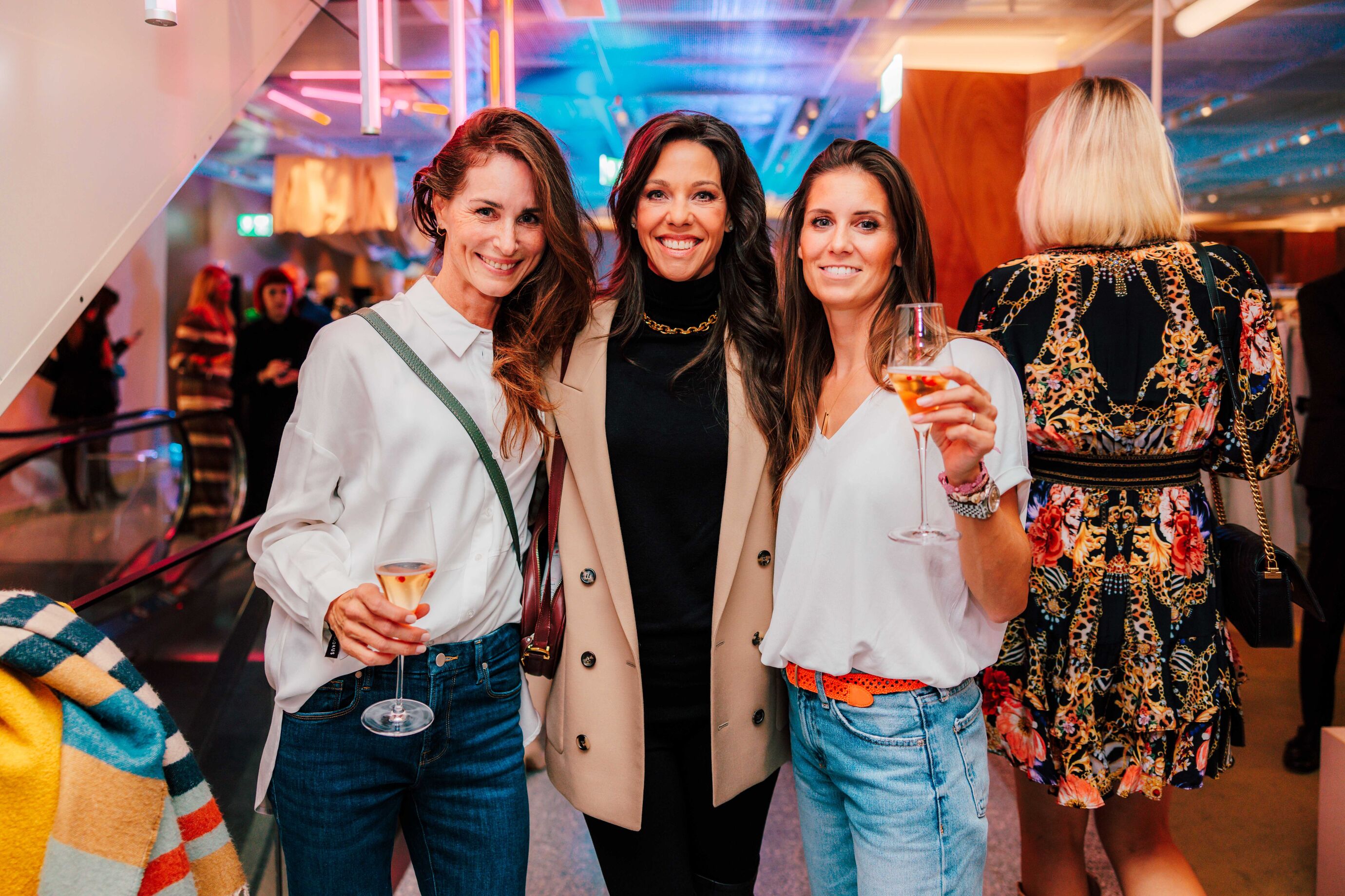 Drei Frauen posieren gemeinsam mit Drinks beim Opening.